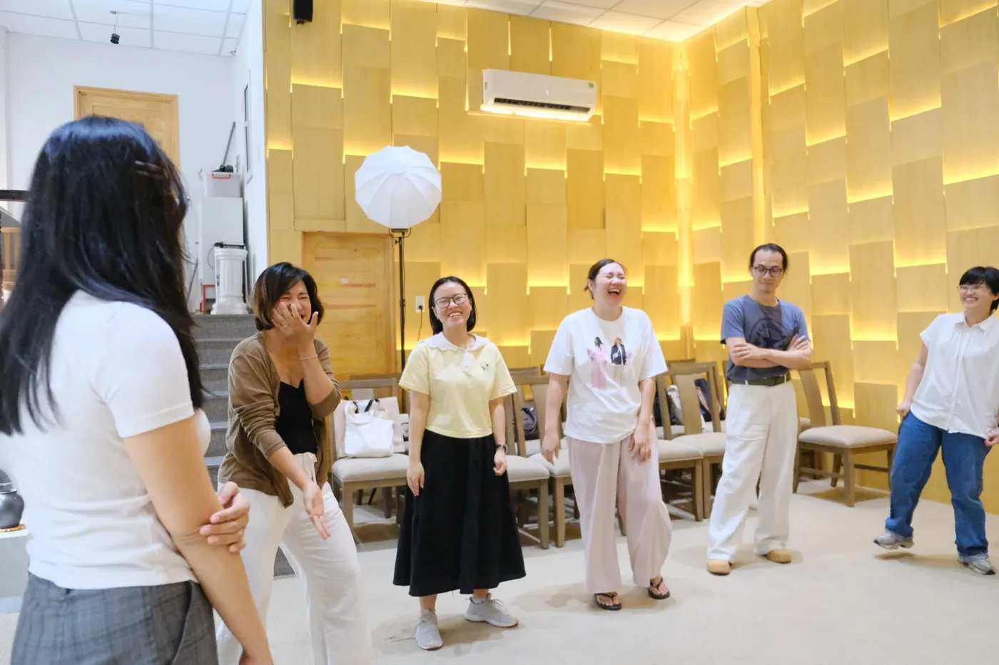 Thành viên đội nhóm đứng thành vòng tròn cười vui trong workshop ứng tác